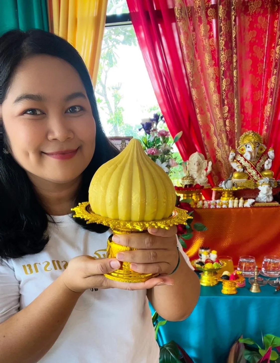ครูทรายถือขนมโมทกะลูกใหญ่บนพานทองหน้าแท่นบูชา
